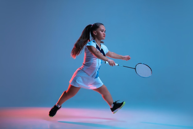 Hermosa mujer enana practicando bádminton aislado en azul en luz de neón