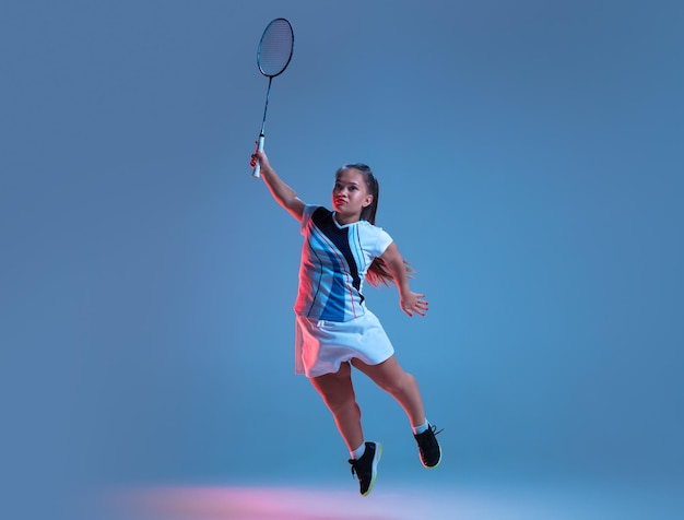 Hermosa mujer enana practicando bádminton aislado en azul en luz de neón