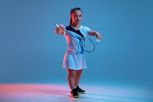 Hermosa mujer enana practicando bádminton aislado en azul en luz de neón