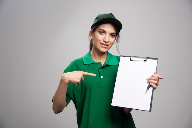 Hermosa mujer de entrega en uniforme verde apuntando al portapapeles.