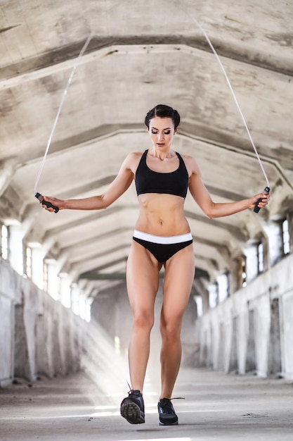 Hermosa mujer en entrenamiento de ropa deportiva con cuerda de saltar en edificio industrial