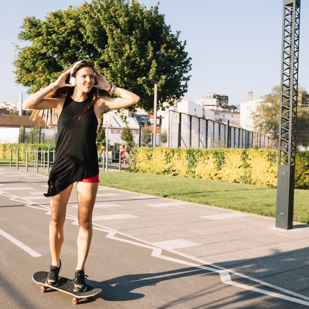 Hermosa mujer escuchando música mientras anda en monopatín en la calle