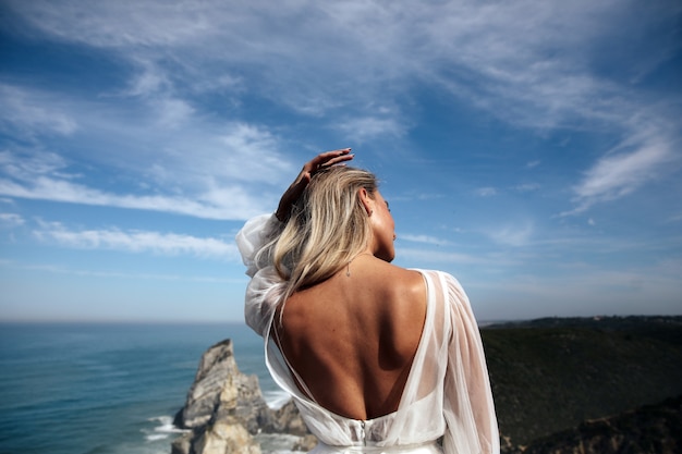 Hermosa mujer con la espalda desnuda se encuentra en la vista panorámica de la costa