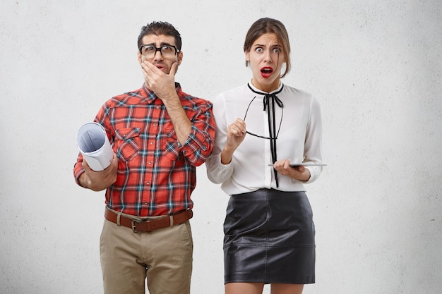 Hermosa mujer estupefacta se quita los anteojos, oye noticias horribles y el nerd masculino mira a través de los anteojos con gran disgusto.