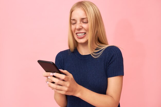 Hermosa mujer europea joven emocional con brackets dentales y pecas charlando en línea con amigos a través de la aplicación en el móvil
