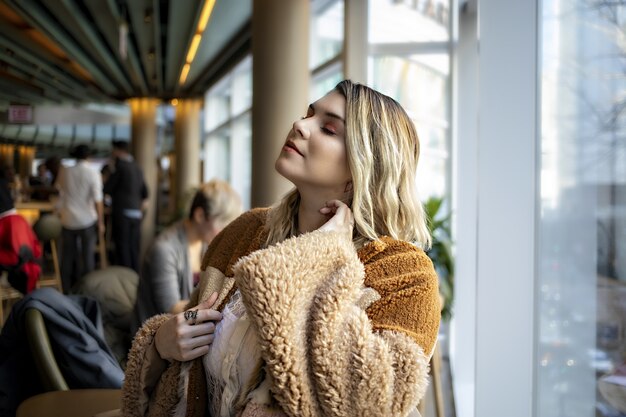 Hermosa mujer europea vistiendo un abrigo naranja de moda y disfrutando de su tiempo en un café