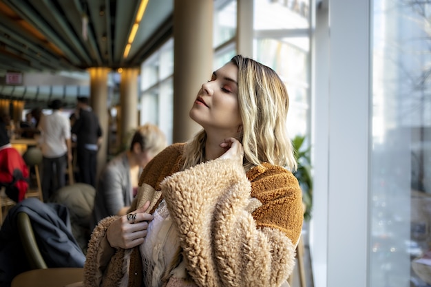 Hermosa mujer europea vistiendo un abrigo naranja de moda y disfrutando de su tiempo en un café