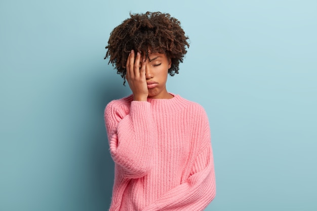 Hermosa mujer con exceso de trabajo siente sueño, cubre la mitad de la cara con la palma, mantiene los ojos cerrados