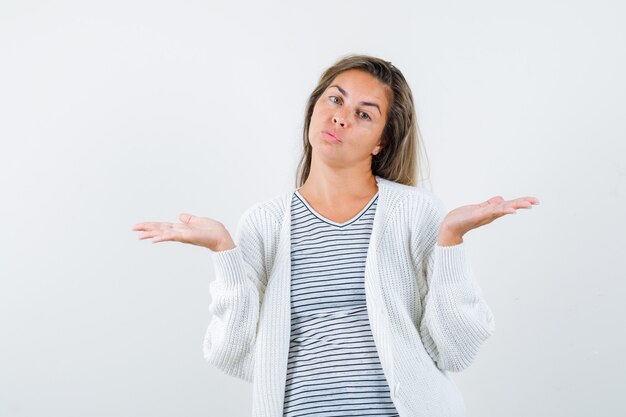 Hermosa mujer extendiendo las palmas a un lado con los labios fruncidos en la chaqueta y mirando tentadora. vista frontal.