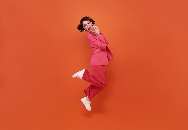Hermosa mujer feliz sonriendo y saltando mientras celebra el éxito aislado sobre fondo naranja