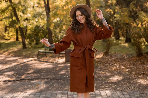 Foto gratuita hermosa mujer flaca sonriente con estilo con el pelo rizado caminando en el parque vestida con abrigo marrón cálido, estilo callejero de moda de otoño