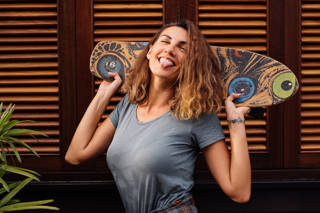 Hermosa mujer en forma en pantalones cortos de jean, camisa a cuadros con longboard