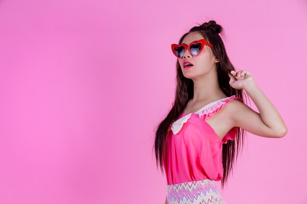 Una hermosa mujer con gafas rojas con un gran sombrero en un rosa.