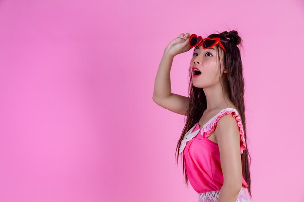 Una hermosa mujer con gafas rojas con un gran sombrero en un rosa.