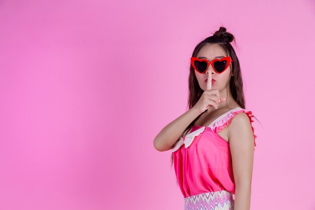 Una hermosa mujer con gafas rojas con un gran sombrero en un rosa.