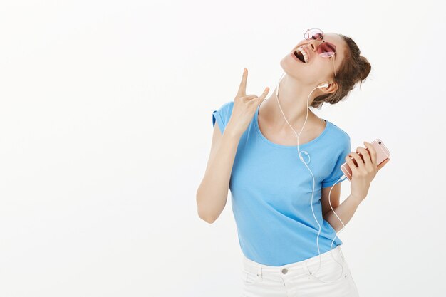 Hermosa mujer con gafas de sol escuchando música en auriculares, mediante teléfono móvil