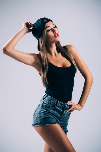 Hermosa mujer con gorra se divierte en una pared gris, sonriendo y mirando hacia un lado.