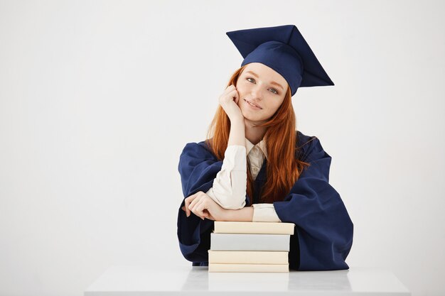 Hermosa mujer graduada sentada con libros sonriendo.