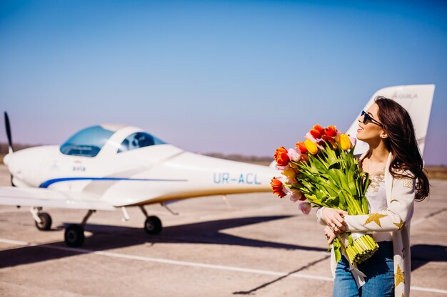 Hermosa mujer con gran ramo de tulipanes se encuentra ante un avión