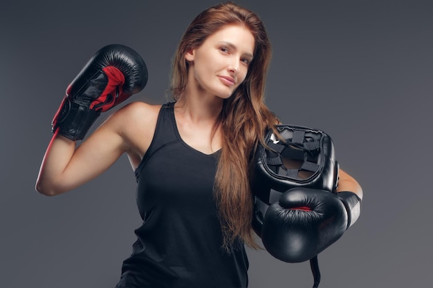 Hermosa mujer con guantes de boxeador sostiene un casco protector mientras posa para el fotógrafo.