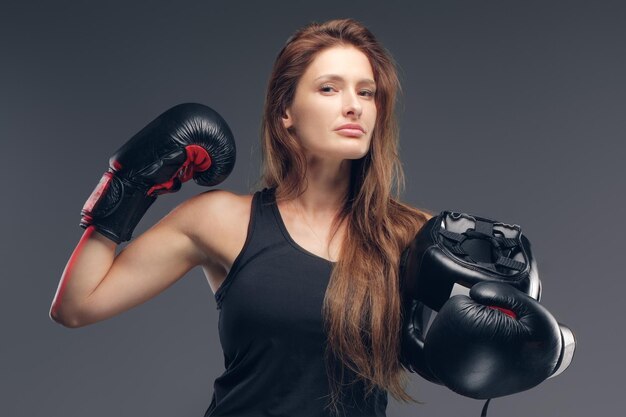 Hermosa mujer con guantes de boxeador sostiene un casco protector mientras posa para el fotógrafo.