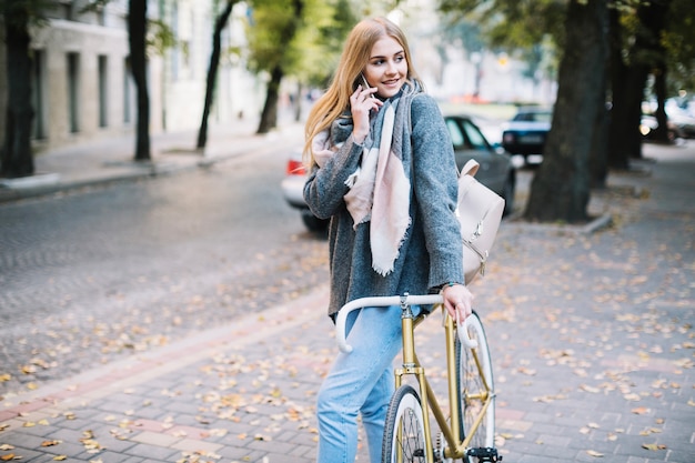 Hermosa mujer hablando por teléfono inteligente cerca de bicicleta