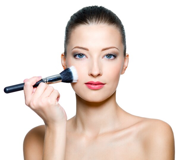 Hermosa mujer haciendo maquillaje en la cara con cepillo cosmético aislado en blanco