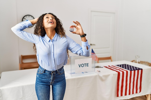 Foto gratuita hermosa mujer hispana parada en la campaña política votando en la boleta sonriendo confiada tocando el cabello con gesto de mano arriba posando atractiva y de moda