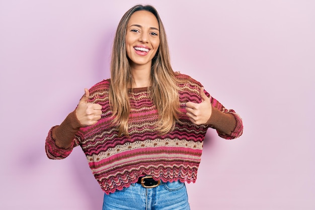 Hermosa mujer hispana con suéter hippie signo de éxito haciendo gesto positivo con los pulgares hacia arriba sonriendo y feliz expresión alegre y gesto de ganador