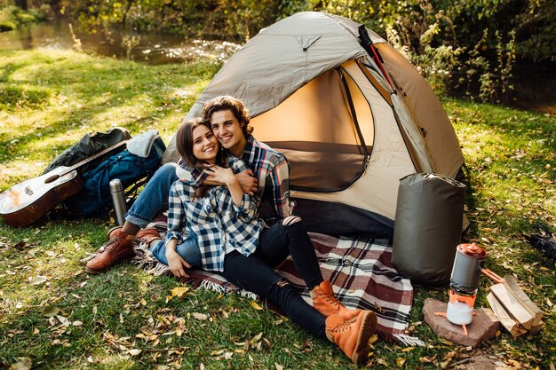 Hermosa mujer y hombre guapo pasar tiempo en la naturaleza, sentado cerca de la carpa en el plaid