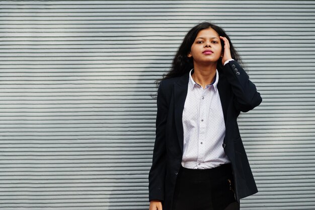 Hermosa mujer india usa una pose formal contra la pared gris