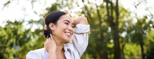 Foto gratuita hermosa mujer joven atando su cabello mientras camina en el parque sonriendo romántico disfrutando de un día cálido