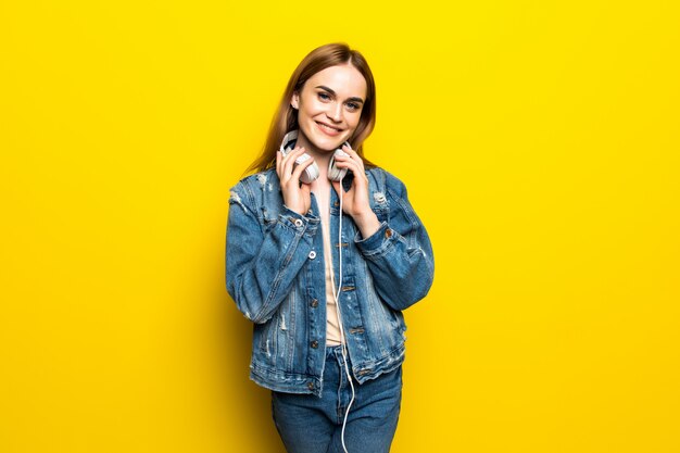 Hermosa mujer joven en auriculares escuchando música y bailando en la pared amarilla