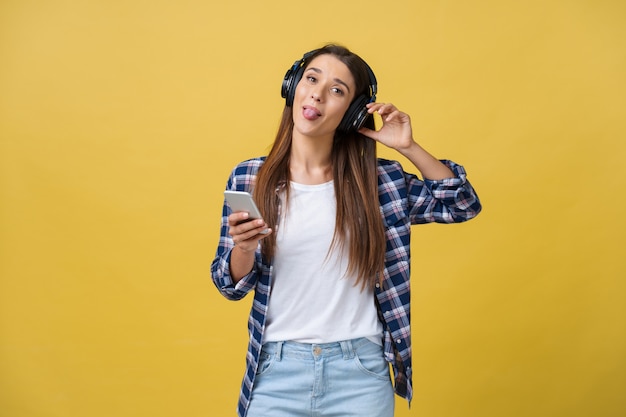 Hermosa mujer joven en auriculares escuchando música y bailando sobre fondo amarillo.