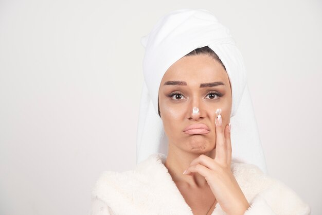 Hermosa mujer joven en una bata de baño blanca posando sobre una pared blanca.