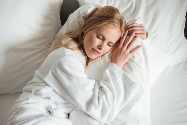 Hermosa mujer joven en bata de baño durmiendo en la cama