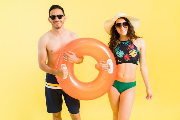 Hermosa mujer joven en bikini y un apuesto hombre encantador compartiendo un salvavidas inflable y a punto de meterse en la piscina durante un día caluroso