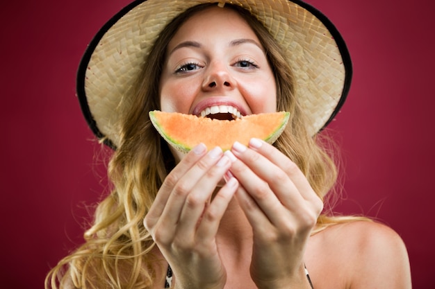 Foto gratuita hermosa mujer joven en bikini comiendo melón. aislado en rojo.