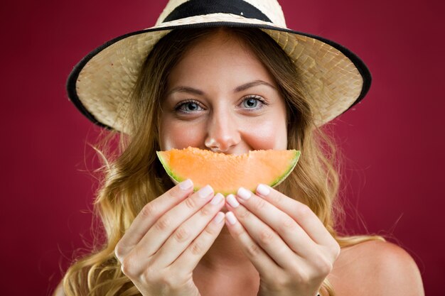 Hermosa mujer joven en bikini comiendo melón. Aislado en rojo.