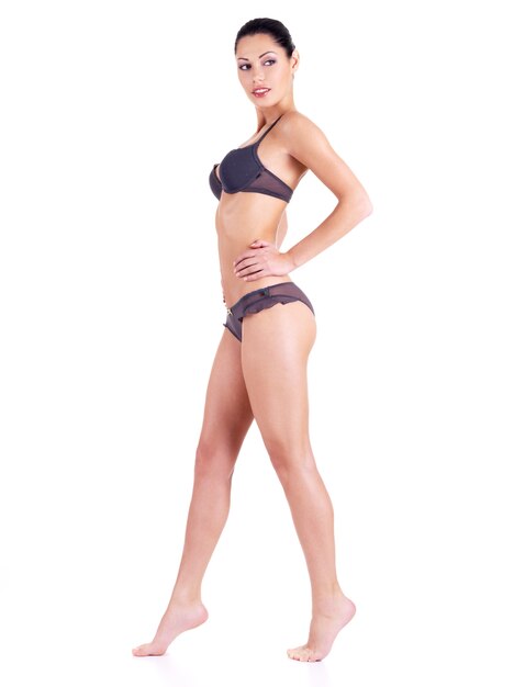 Hermosa mujer joven en bikini gris con piernas largas que se encuentran aisladas en blanco. Retrato de cuerpo entero