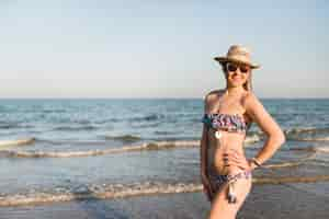 Foto gratuita hermosa mujer joven en bikini de pie frente al mar contra el cielo azul