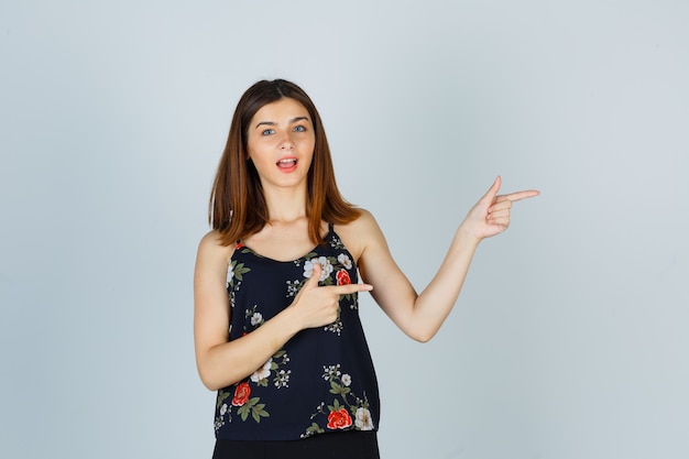 Hermosa mujer joven en blusa, falda apuntando a la derecha y mirando sorprendido