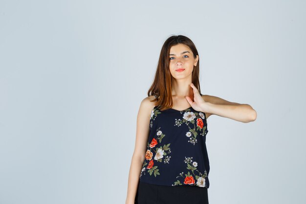 Hermosa mujer joven en blusa, falda posando mientras toca su cuello