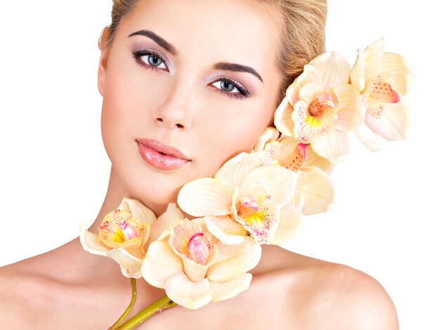 Hermosa mujer joven y bonita con una piel sana y flores cerca de la cara - aislado en blanco