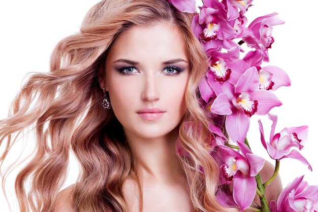 Hermosa mujer joven y bonita con piel sana y flores rosadas cerca de la cara - aislado en blanco.