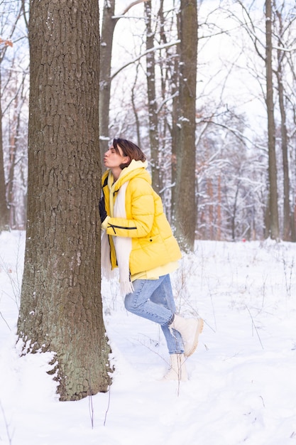 Hermosa mujer joven en el bosque de invierno muestra tiernos sentimientos por la naturaleza, muestra su amor por el árbol