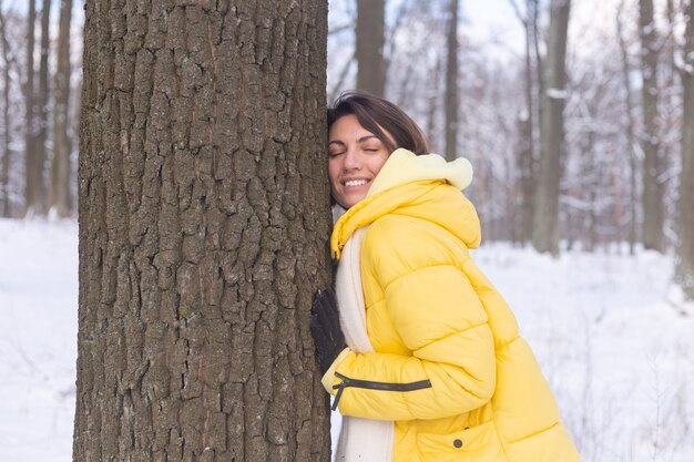 Hermosa mujer joven en el bosque de invierno muestra tiernos sentimientos por la naturaleza, muestra su amor por el árbol