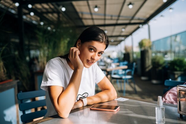 Hermosa mujer joven en un café sosteniendo un teléfono inteligente en sus manos