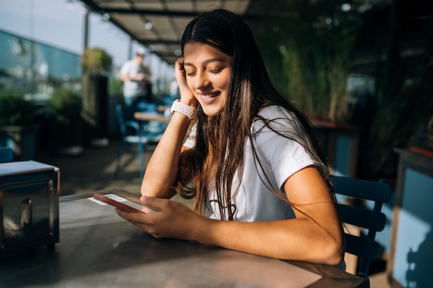 Hermosa mujer joven en un café sosteniendo un teléfono inteligente en sus manos