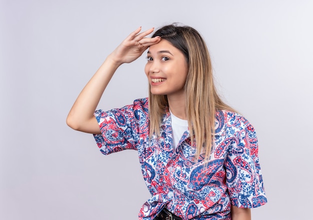 Foto gratuita una hermosa mujer joven con camisa estampada de paisley mirando lejos y buscando algo en una pared blanca